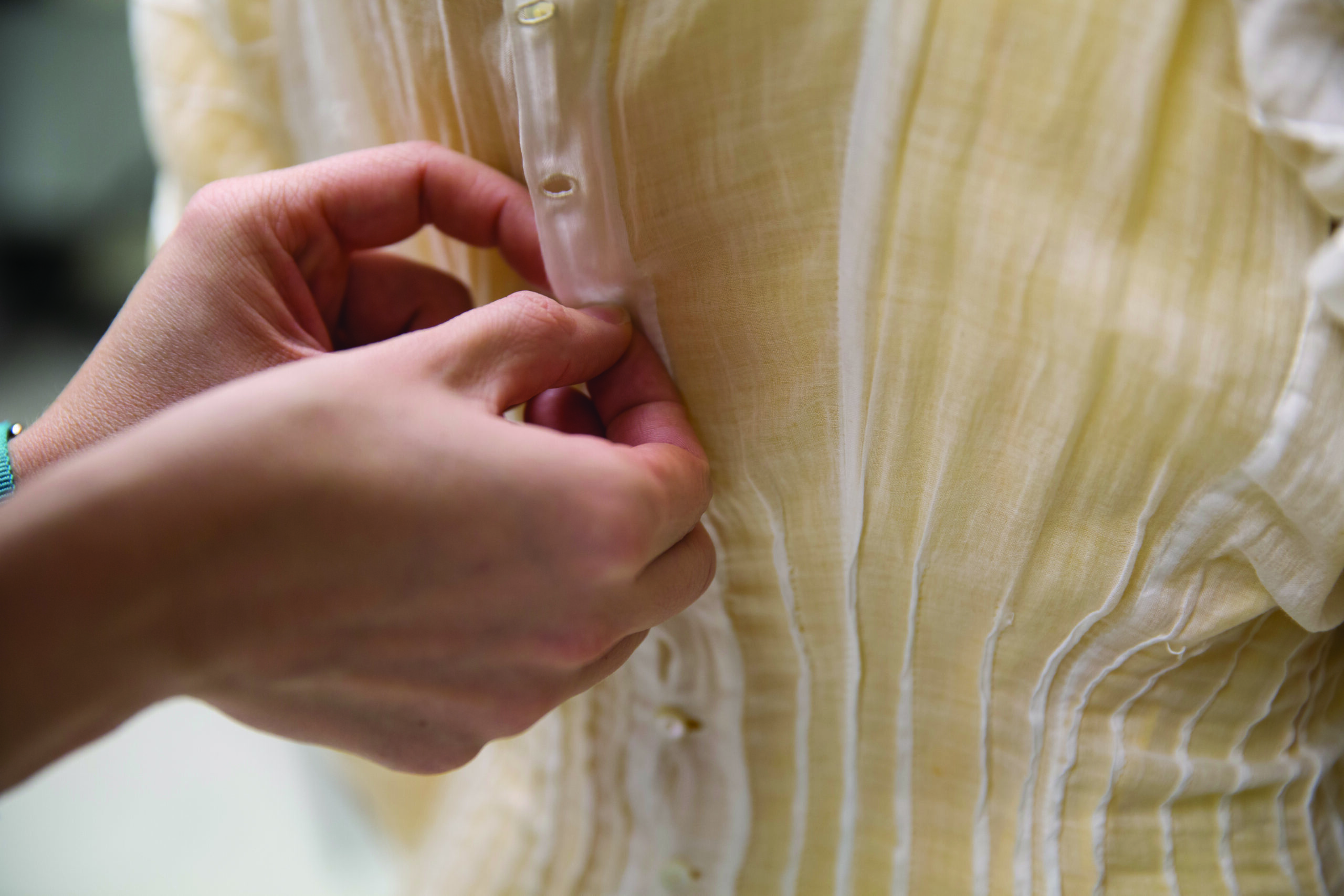 hands buttoning up a garment on a form